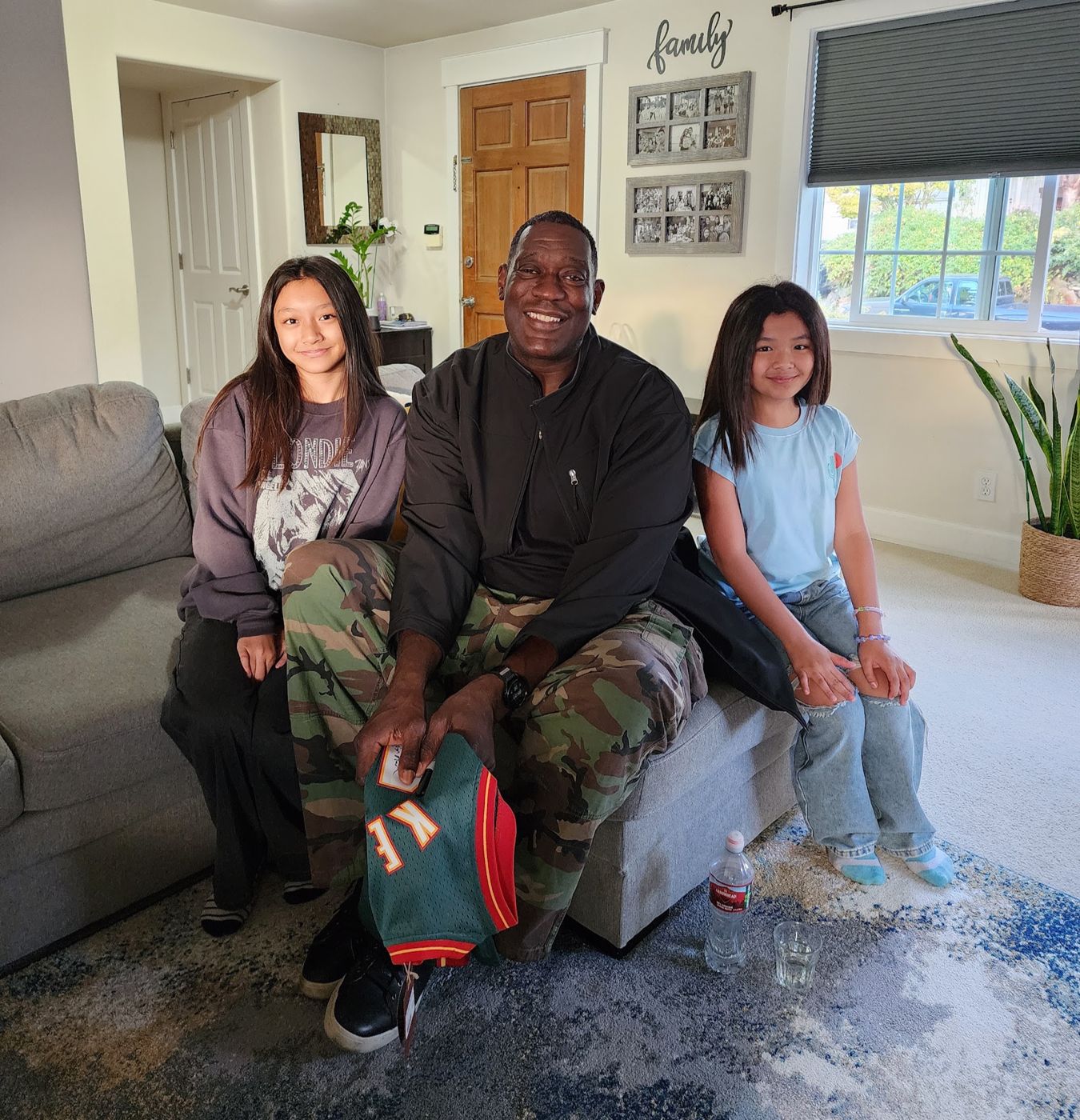 Shawn Kemp on a couch between two girls, holding a Sonics jersey